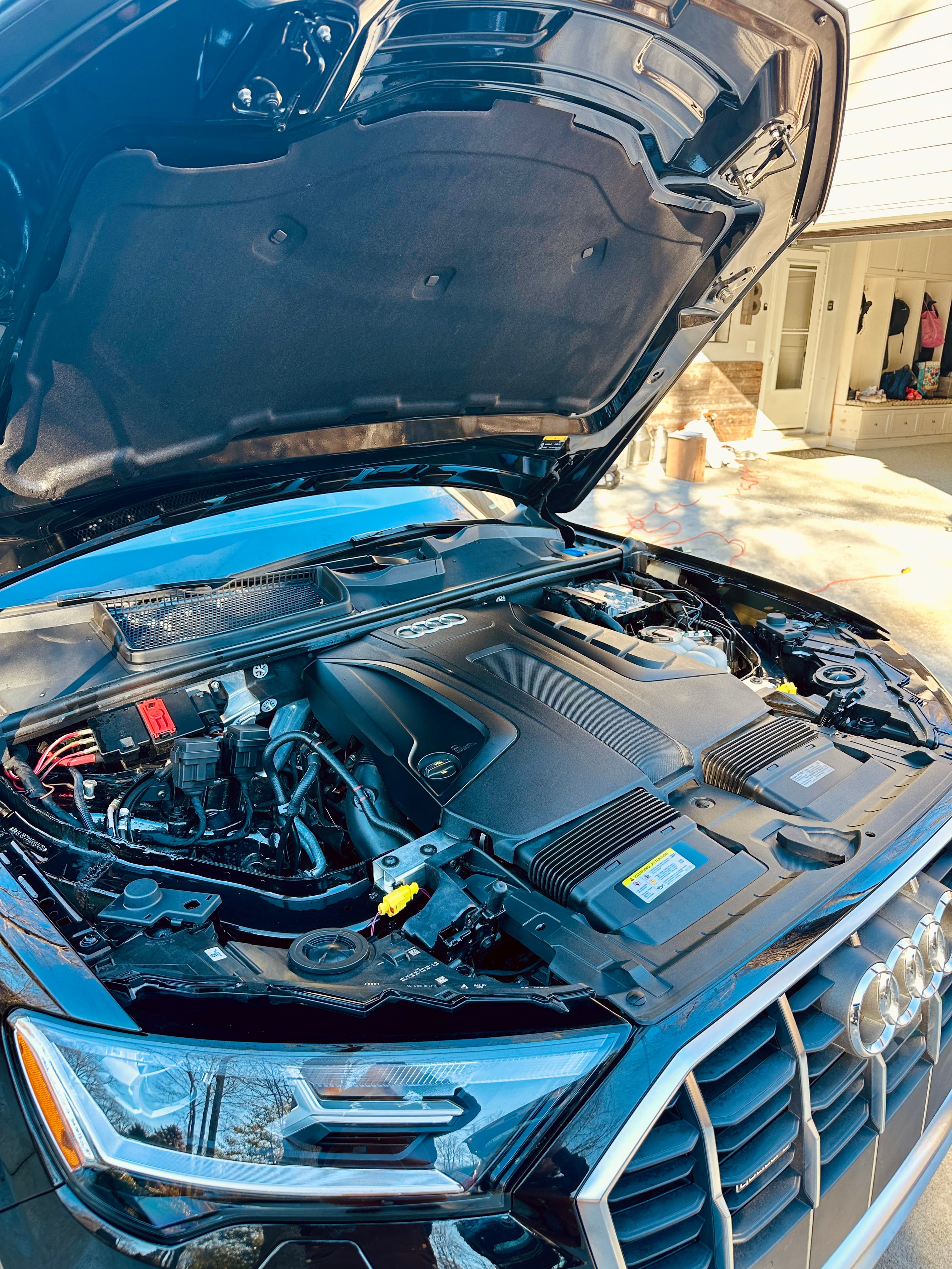 Open hood of a black Audi car revealing a clean engine bay with plastic covers.