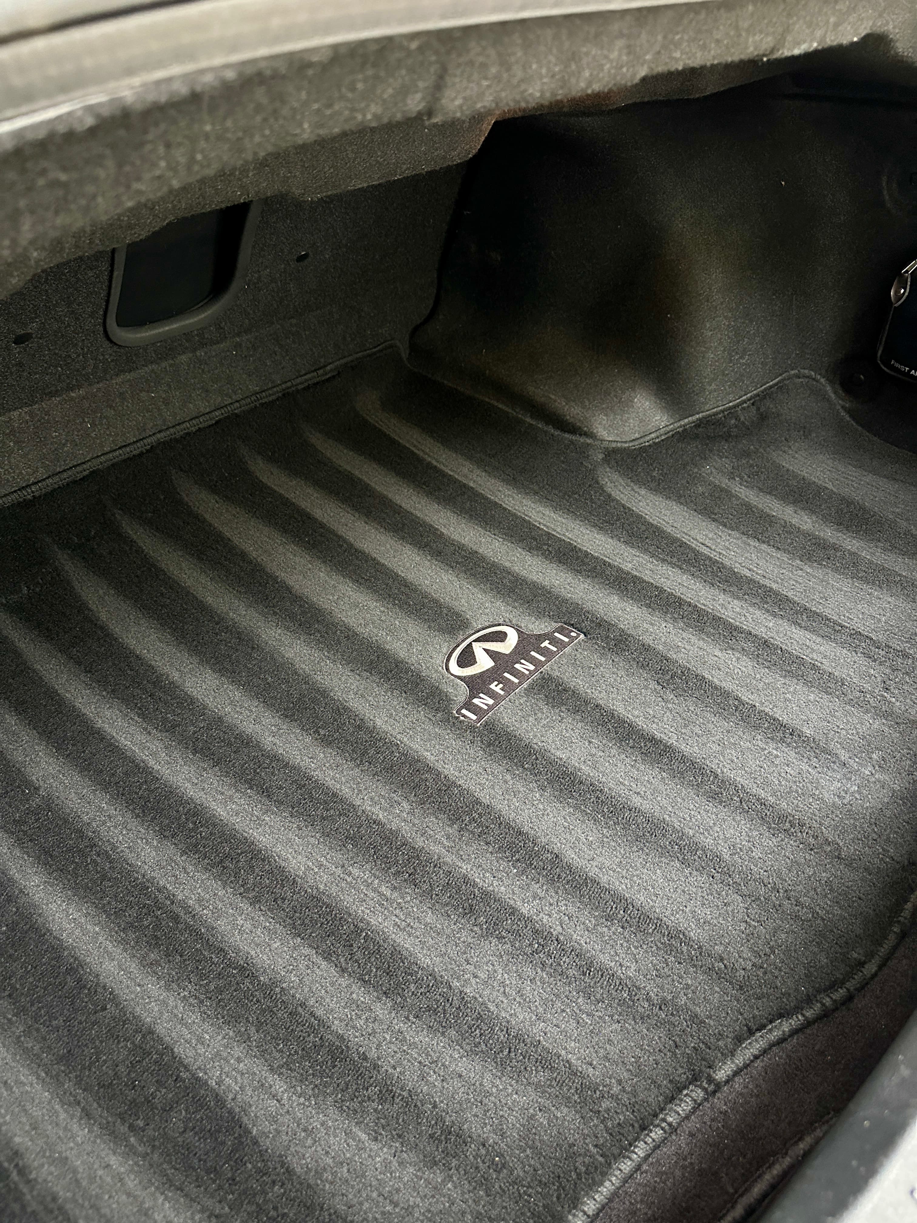 Freshly vacuumed black carpeted Infiniti trunk mat featuring the brand logo and clean vacuum lines.