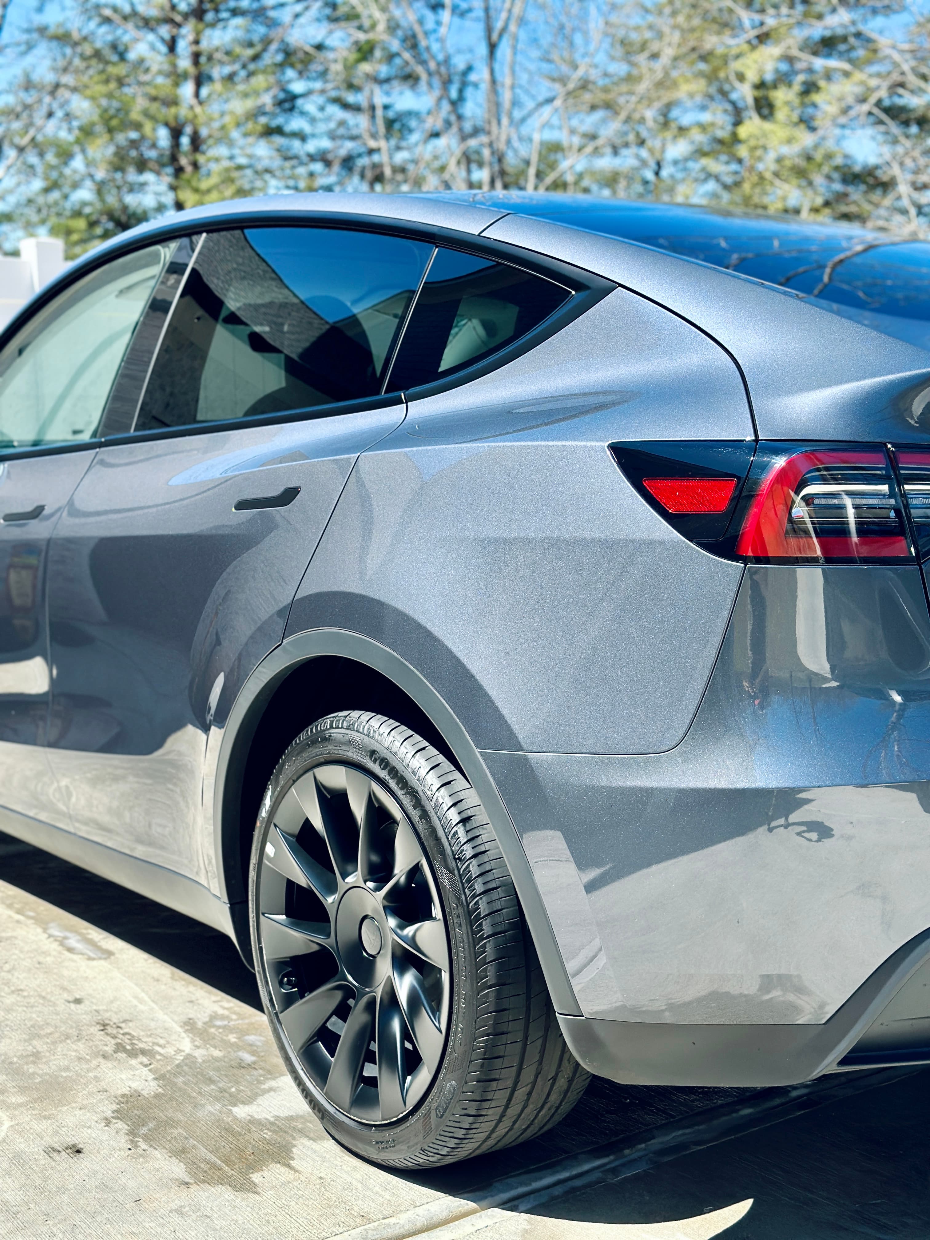 Metallic grey Tesla Model Y featuring black turbine wheels and tinted windows parked on concrete.