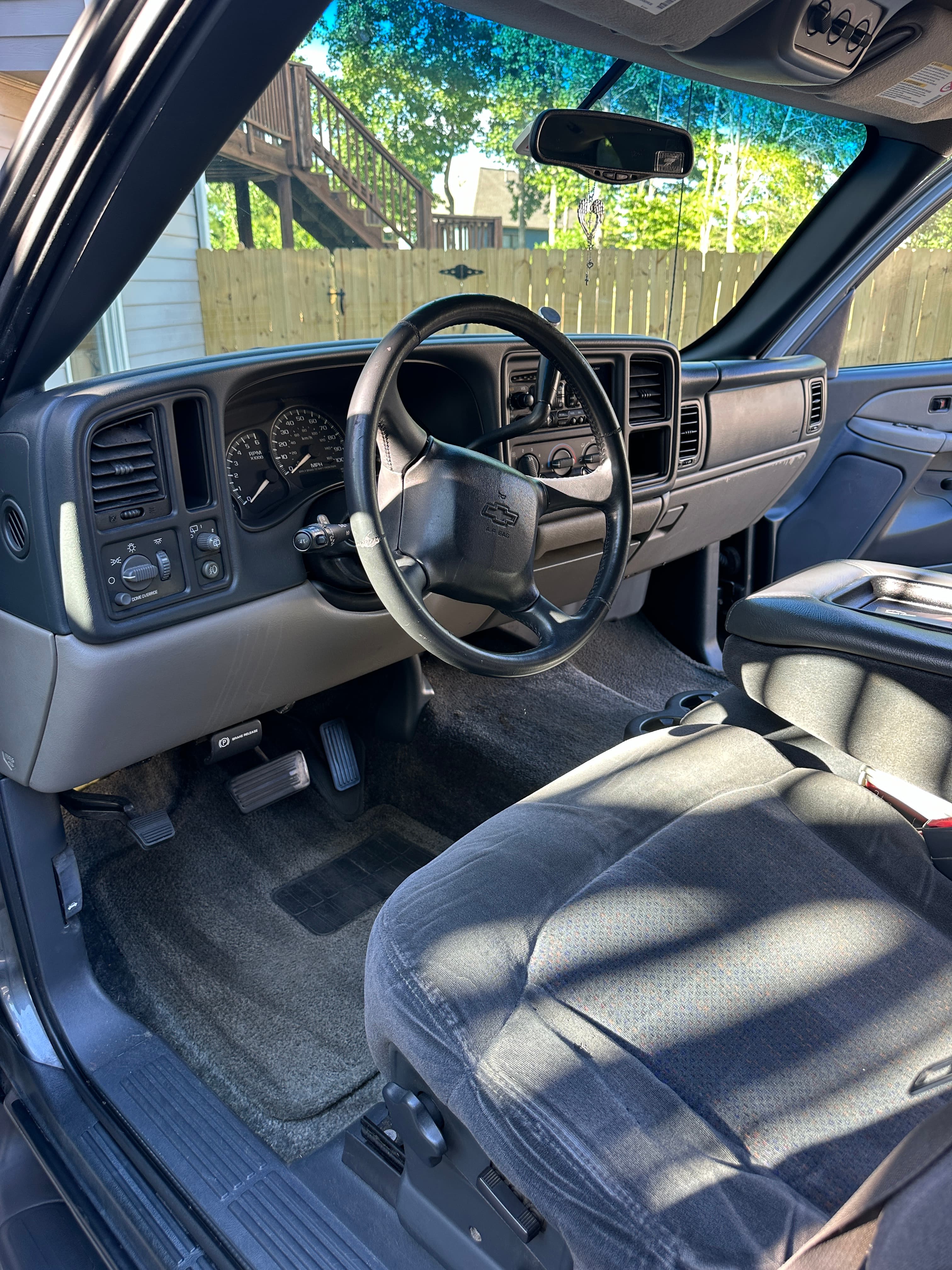 Driver's side interior of a Chevrolet truck with a black steering wheel and gray upholstery.