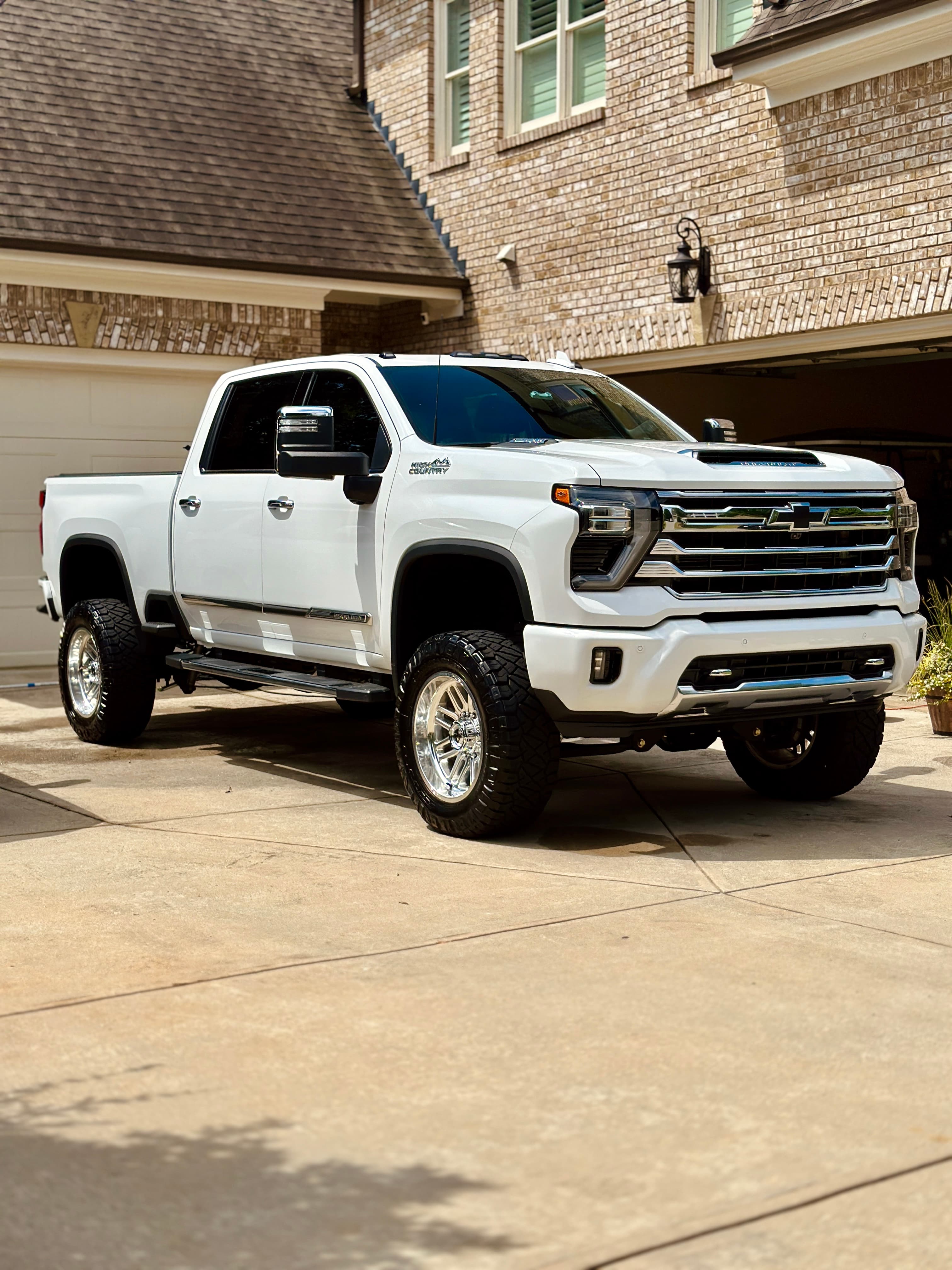 White lifted Chevrolet Silverado High Country truck with chrome wheels parked on a driveway.